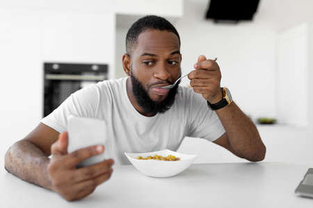 Black man rushing to work eating cereal at homeの写真素材