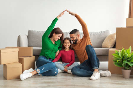 Cheerful parents making symbolic roof of hands above happy daughter