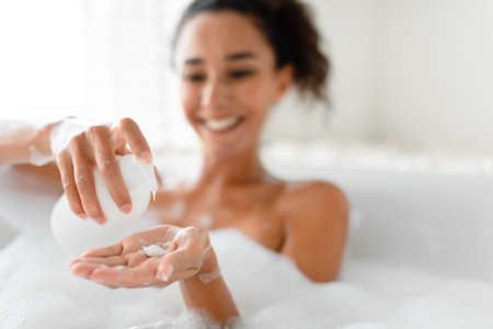Pretty millennial woman using soap while lying in foamy bath at home, selective focus