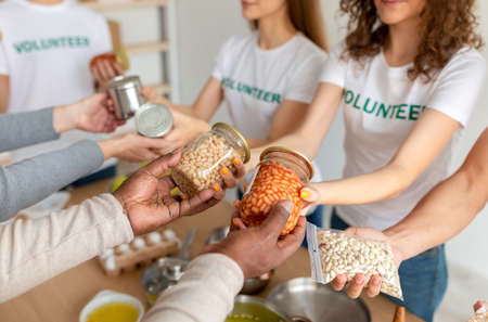 Young group of volunteers giving food donation for poor and elderly people, holding canned food, closeupの写真素材