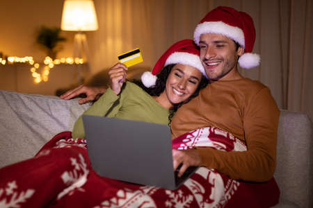 Couple Doing Christmas Shopping Using Laptop And Credit Card Indoors