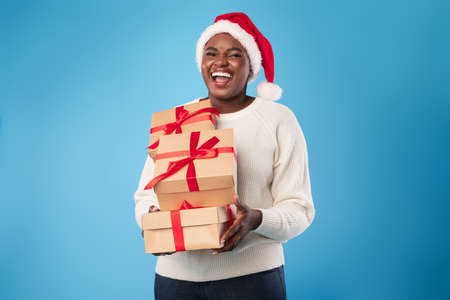African Lady Holding Christmas Presents Wearing Santa Hat, Blue Backgroundの写真素材