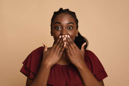 Excited black lady looking at camera, covering her mouthの写真素材