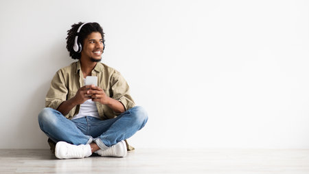 Cheerful Black Guy Using Smartphone And Wireless Headphones For Listening Music Onlineの写真素材