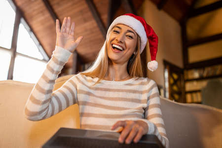 Happy Woman In Santa Hat Waving At Laptop At Homeの写真素材