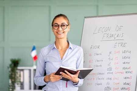 Learning and knowledge concept. Young smiling woman posing near whiteboard with French language...