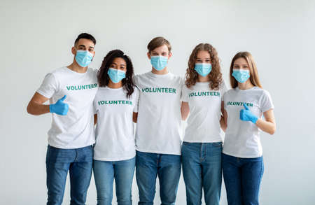 Group of happy multiracial people in masks and gloves showing thumbs up while posing over light studio wallの写真素材