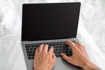 Unrecognizable hands of european millennial male typing on laptop with empty screen in bedの写真素材