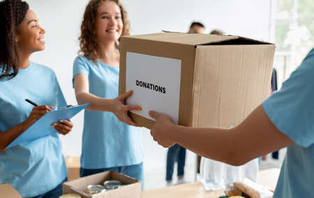 Male volunteer giving box with donations to woman, social worker making notes in clipboard, working in charity centerの写真素材