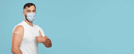 Mature caucasian guy in protective mask show thumb up, arm with plaster aid after injectionの写真素材