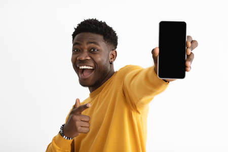 Cheerful black man showing smartphone with empty screenの写真素材