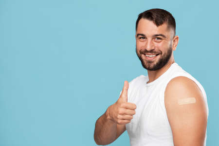 Happy mature caucasian male with beard showing thumb up and shoulder with plaster aid after injectionの写真素材