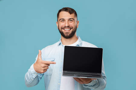 Happy middle aged caucasian guy shows finger at laptop with blank screen, recommends computerの写真素材