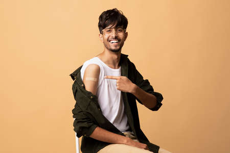 Positive hindu guy pointing at medical band on his shoulderの写真素材