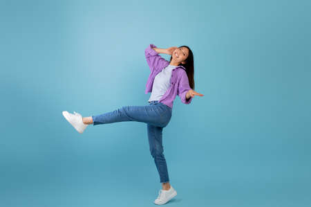 Having fun. Joyful asian lady dancing and fooling around, being in a good mood, celebrating triumph, blue backgroundの写真素材