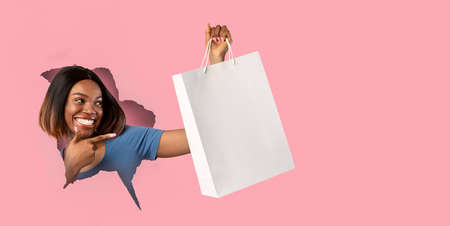 Black woman holding pointing at shopper bag through paper holeの写真素材