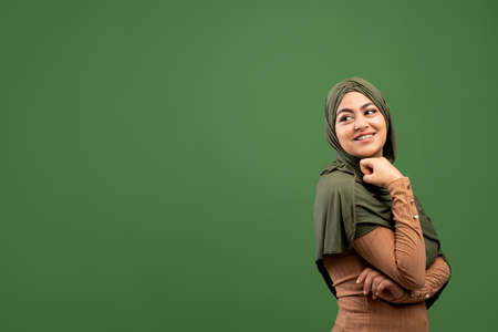 Young islamic lady in hijab looking back at copy space over dark green background, free space, studio shotの写真素材