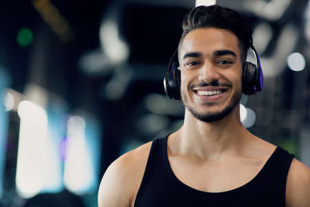 Portrait Of Happy Athletic Arab Man Wearing Wireless Headphones Posing In Gymの写真素材