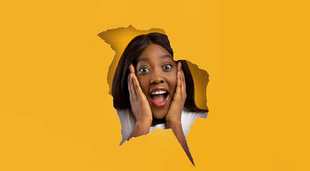 Surprised shocked black woman looking through paper hole
