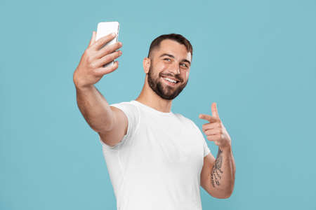 Smiling handsome adult european guy blogger points finger to smartphone webcam, streaming video
