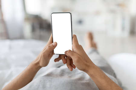 Unrecognizable Guy Using Smartphone With Blank White Screen While Lying In Bedの写真素材