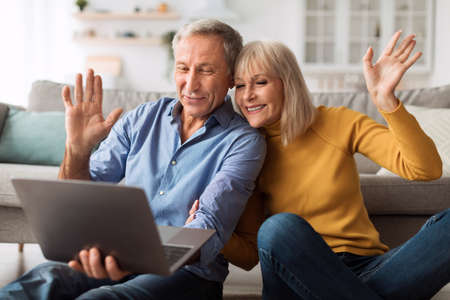Senior Couple Making Video Call Waving Hand To Laptop Indoors