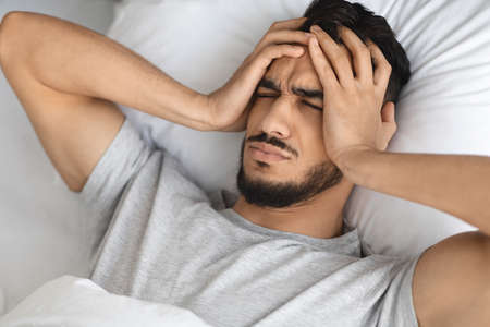Migraine Concept. Young Arab Man Waking Up In Bed With Acute Headacheの写真素材