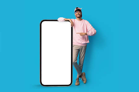 Stylish indian guy standing by huge smartphone with blank screen