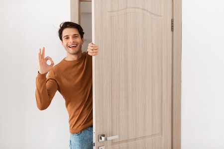 Cheerful guy looking out of door showing okay gestureの写真素材
