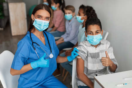 Nurse And Vaccinated Boy Gesturing Thumbs-Up After Vaccination In Clinicの写真素材