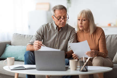 Senior Couple Looking Through Papers Counting Reading Bills At Homeの写真素材