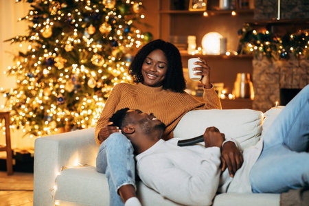 Lovely black woman spending time with her happy boyfriend on Christmas eve in decorated living room, copy spaceの写真素材