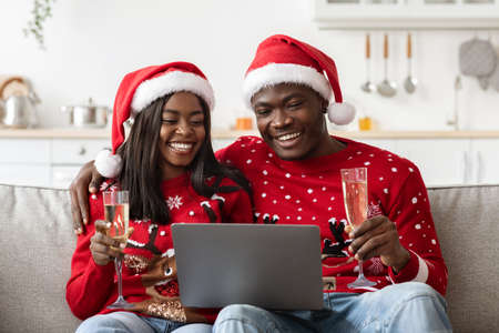 Happy black couple having online New Year party, using laptopの写真素材