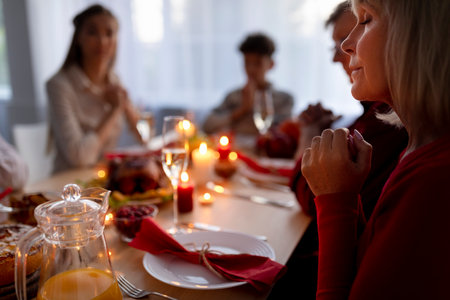 Elderly lady and her extended family praying, expressing thanks to God, sitting at table with festive meal at homeの写真素材