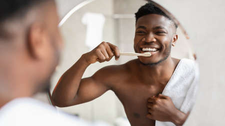 Cheerful African American Man Cleaning Teeth Near Mirror In Bathroom