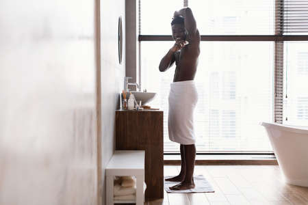 African American Man Applying Antiperspirant On Armpits In Modern Bathroomの写真素材