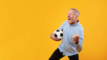Mature man posing with soccer ball on yellow backgroundの写真素材