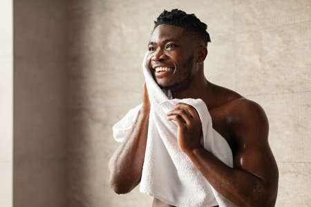 Handsome Black Man Wiping Face With Towel In Modern Bathroomの写真素材