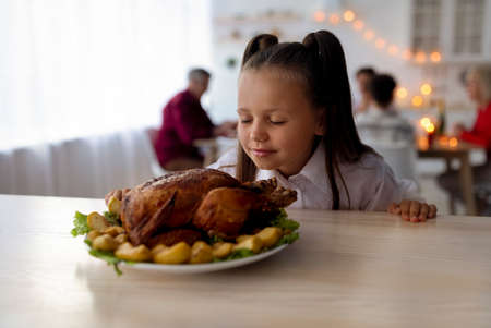 Little girl smelling yummy roasted turkey, having festive Thanksgiving or Christmas dinner with family in dining roomの写真素材