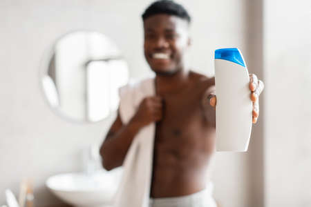 African American Man Showing Shampoo Bottle Standing In Modern Bathroomの写真素材