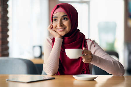 Dreamy middle eastern woman sitting at table with digital tabletの写真素材