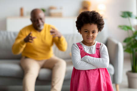 Disgruntled black small girl with crossed arms on chest does not want listen to old man, explains somethingの写真素材