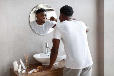 African Man Cleaning Teeth In Morning Using Toothbrush In Bathroomの写真素材