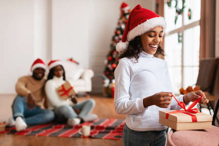 Happy black girl celebrating Christmas unwrapping gift boxの写真素材