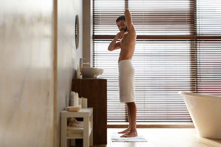 Handsome young guy using applying deodorant in bathroomの写真素材
