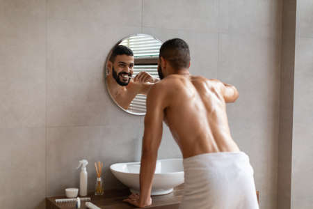 Happy young Arab man using toothbrush in bathroomの写真素材
