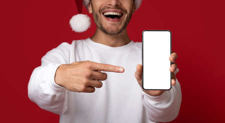 Mobile Mockup. Cheerful Man In Santa Hat Pointing At Blank Smartphone Screenの写真素材