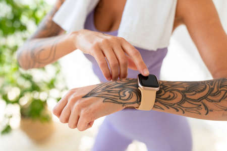 Young tattooed woman looking at activity fitness tracker during workout break, checking heart rate and burned caloriesの写真素材