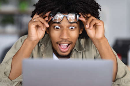 Excited African American Guy Taking Off Eyeglasses And Looking At Laptop Screenの写真素材