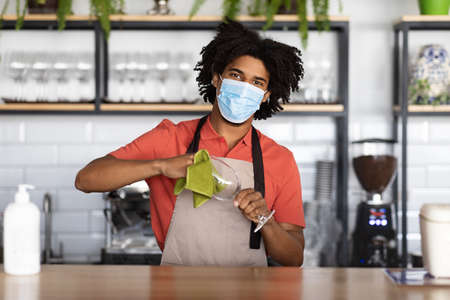 Work During Pandemic. Young black bartender wearing medical mask standing at bar counterの写真素材
